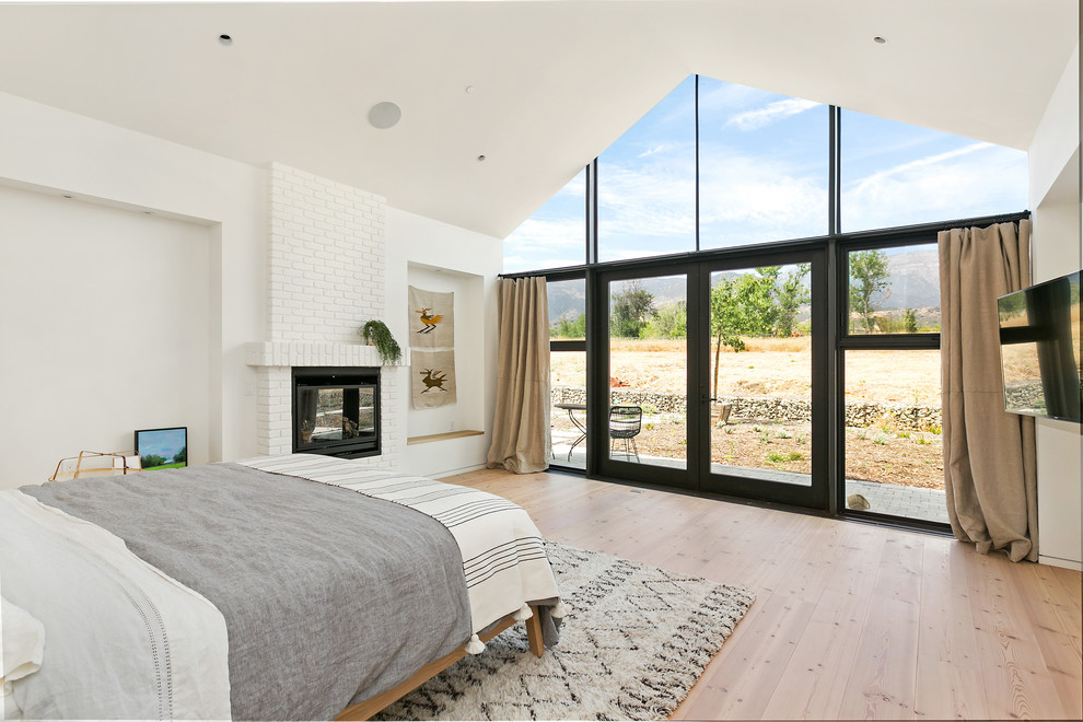 Exemple d'une chambre parentale nature avec un mur blanc, un sol en bois brun, une cheminée standard, un manteau de cheminée en brique et un sol marron.