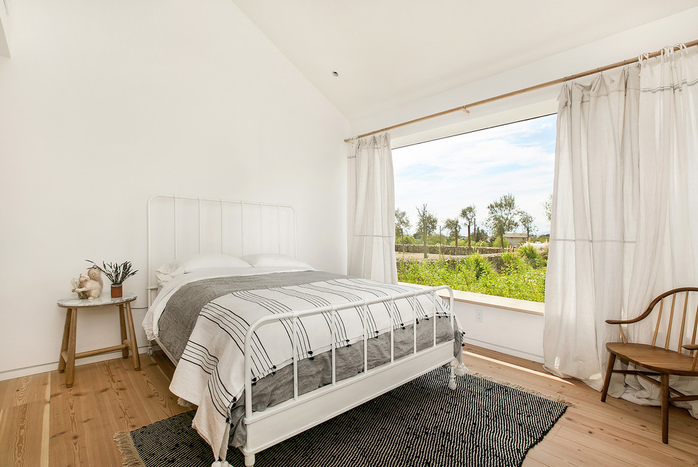 Foto på ett lantligt sovrum, med vita väggar, mellanmörkt trägolv och brunt golv