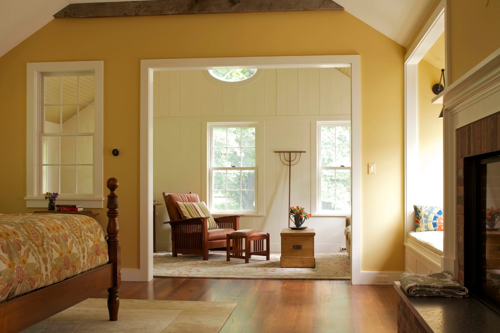 Großes Landhausstil Hauptschlafzimmer mit gelber Wandfarbe, braunem Holzboden, Kamin und Kaminumrandung aus Backstein in New York