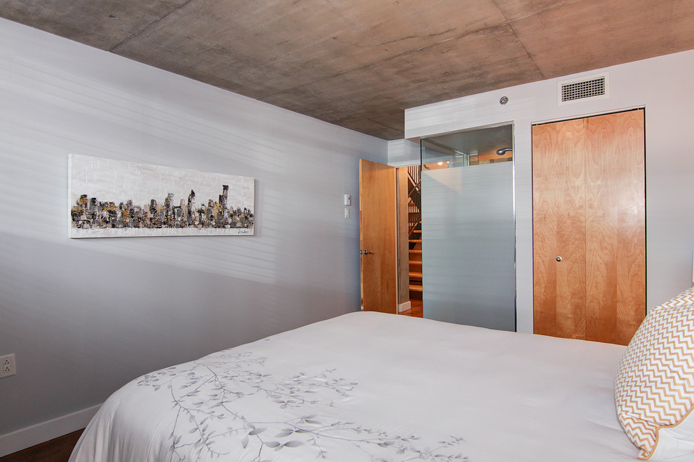 Foto di una camera matrimoniale industriale di medie dimensioni con pareti grigie e pavimento in legno massello medio