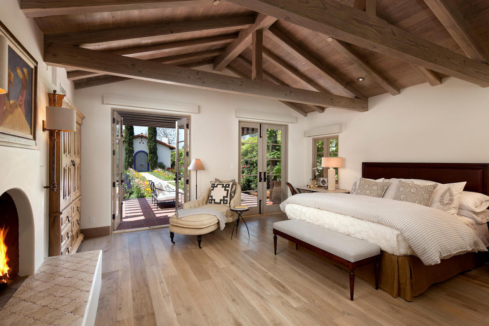Ejemplo de dormitorio mediterráneo con paredes beige, suelo de madera clara y todas las chimeneas