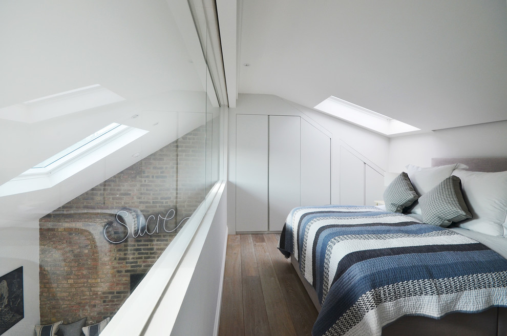Photo of a small contemporary mezzanine loft bedroom in London with white walls, light hardwood flooring and no fireplace.