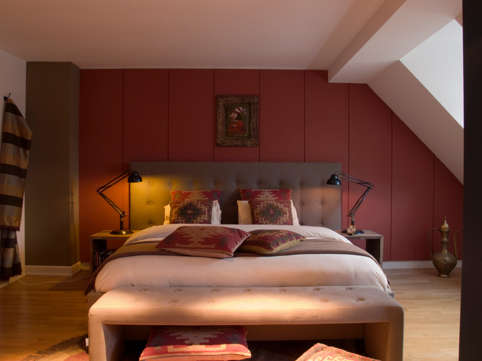 Modelo de dormitorio bohemio sin chimenea con paredes rojas, suelo de madera clara y suelo beige
