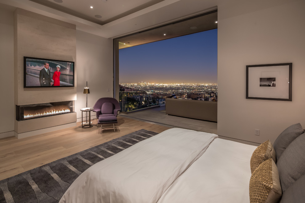 Modernes Hauptschlafzimmer mit beiger Wandfarbe, hellem Holzboden, Gaskamin und Kaminumrandung aus Stein in Los Angeles