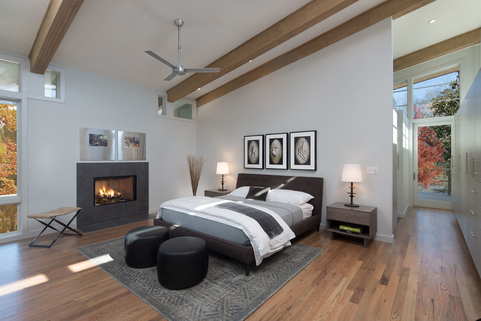 Idée de décoration pour une chambre parentale design de taille moyenne avec un mur gris, un sol en bois brun, une cheminée standard et un manteau de cheminée en carrelage.