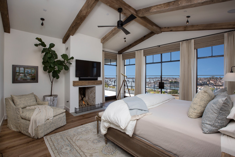 This is an example of a large guest bedroom in Los Angeles with white walls, medium hardwood flooring, a standard fireplace and a plastered fireplace surround.