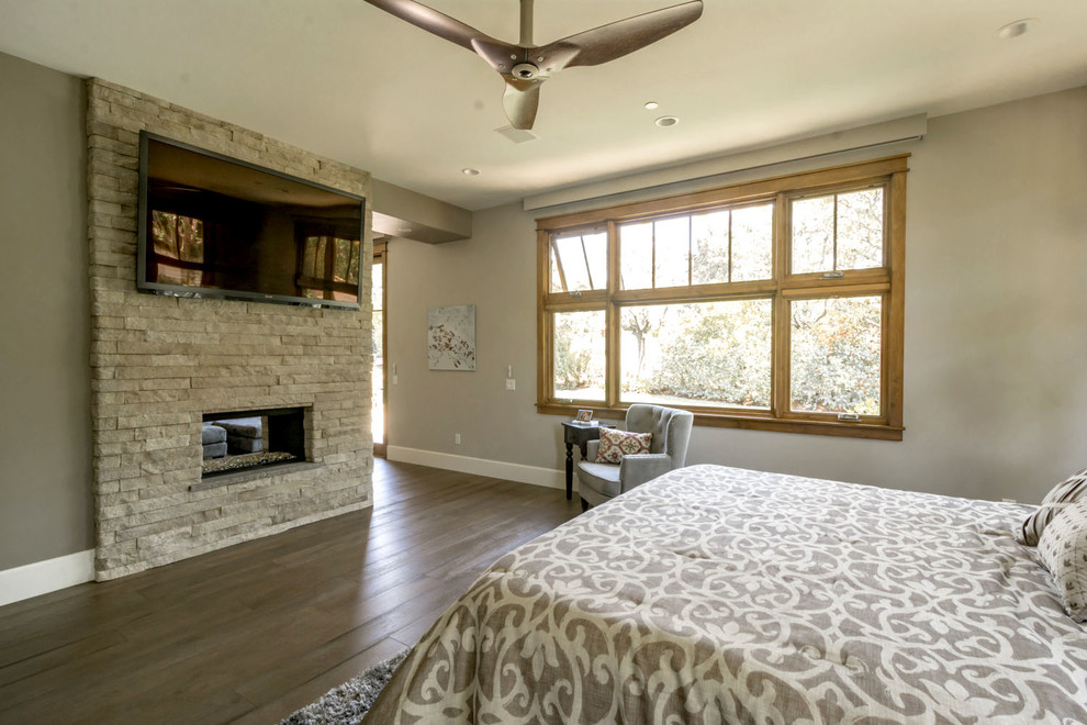 Foto de dormitorio principal de estilo americano extra grande con paredes grises, suelo de madera en tonos medios, todas las chimeneas, marco de chimenea de piedra y suelo gris