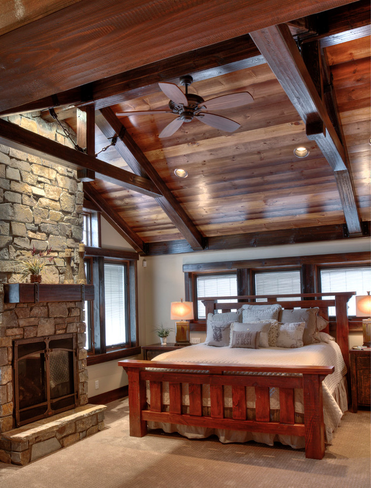 Idée de décoration pour une grande chambre chalet avec un mur beige, une cheminée standard et un manteau de cheminée en pierre.