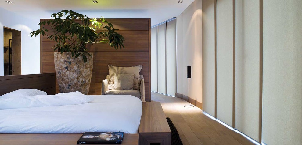 Imagen de dormitorio principal actual grande con paredes blancas, suelo de madera clara y suelo marrón