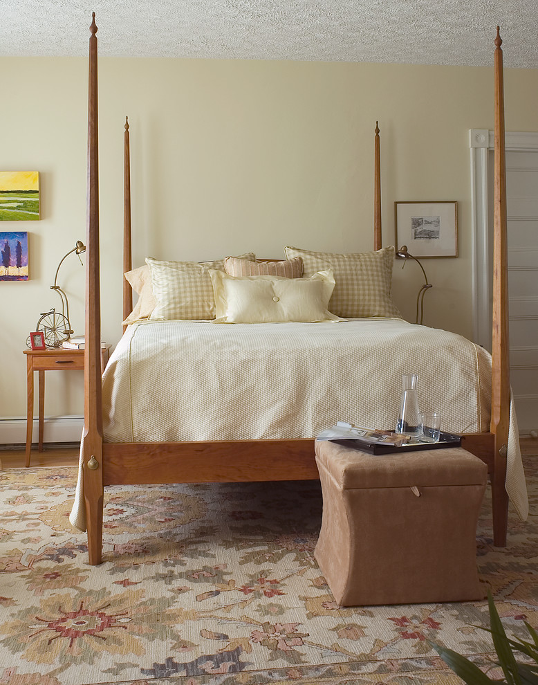 This is an example of a medium sized traditional master bedroom in Portland Maine with yellow walls, medium hardwood flooring and no fireplace.