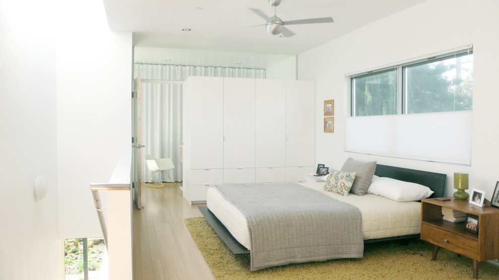 Cette photo montre une chambre mansardée ou avec mezzanine moderne avec un mur blanc et un sol en bois brun.