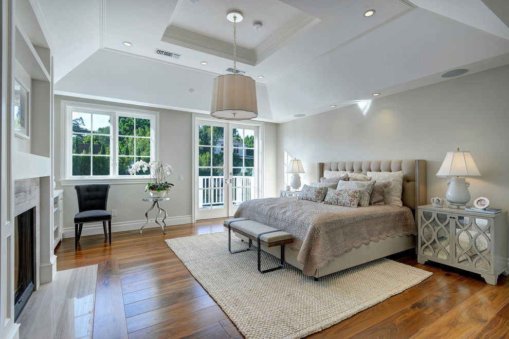 Immagine di una camera da letto classica con pareti grigie, pavimento in legno massello medio e camino classico