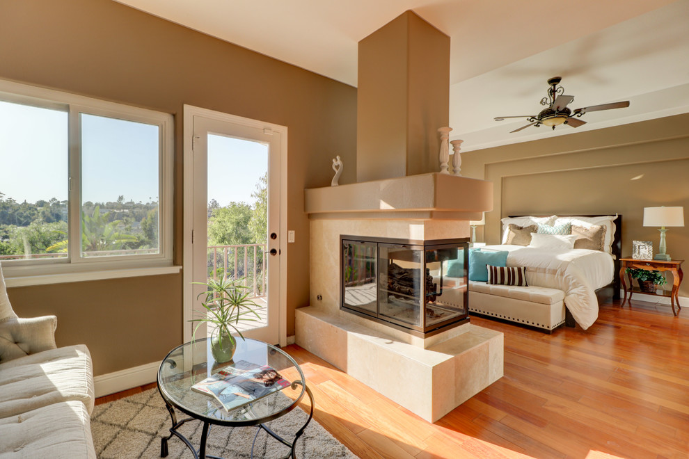 Mediterranes Hauptschlafzimmer mit brauner Wandfarbe, braunem Holzboden, Tunnelkamin und orangem Boden in Orange County