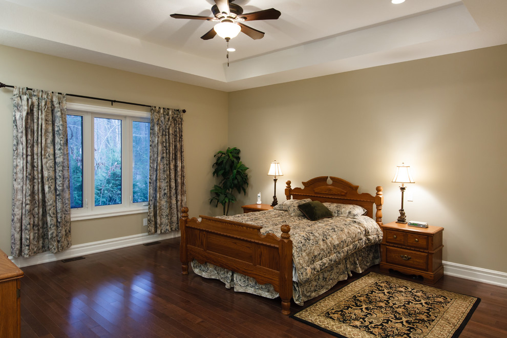 Large traditional master bedroom in Toronto with beige walls and dark hardwood flooring.