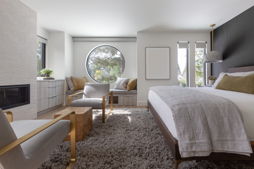 Diseño de dormitorio contemporáneo con paredes blancas, suelo de madera en tonos medios, chimenea lineal, marco de chimenea de baldosas y/o azulejos y suelo marrón