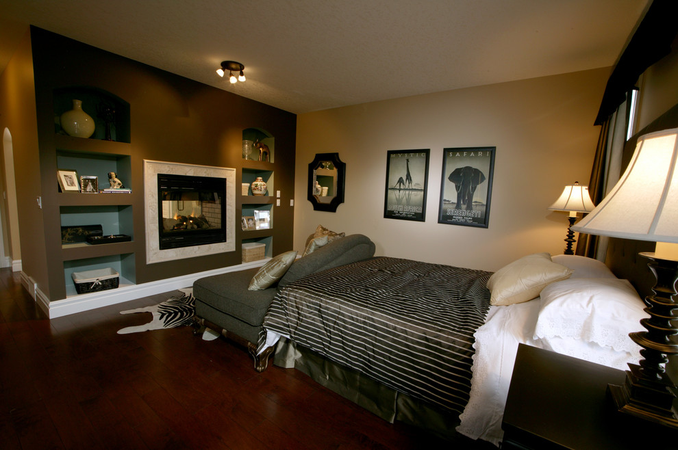 Imagen de dormitorio principal tradicional renovado de tamaño medio con paredes beige, suelo de madera en tonos medios, chimenea de doble cara y marco de chimenea de piedra