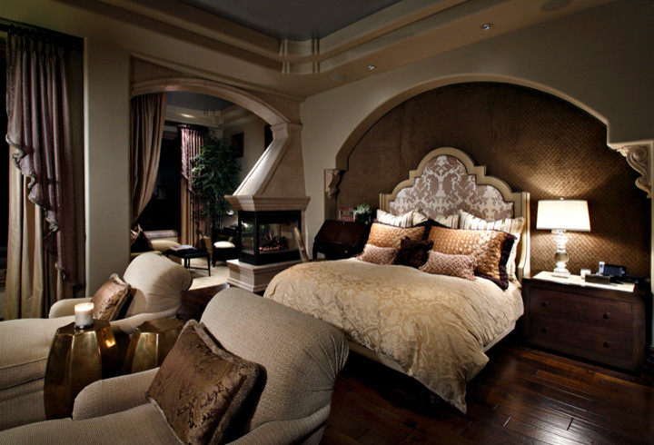 Modelo de dormitorio principal tradicional con paredes marrones, suelo de madera oscura y chimenea de doble cara
