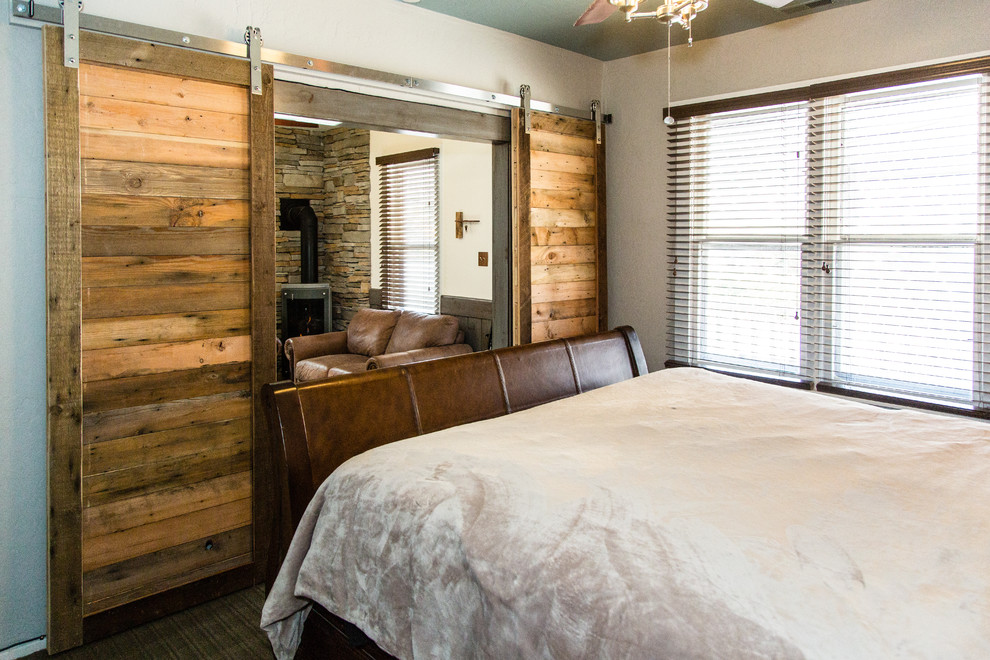 Design ideas for a small rustic master bedroom in Salt Lake City with white walls, carpet, a wood burning stove, a stone fireplace surround and brown floors.