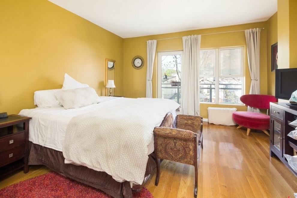 Cette photo montre une chambre parentale moderne de taille moyenne avec un mur jaune et un sol en bois brun.