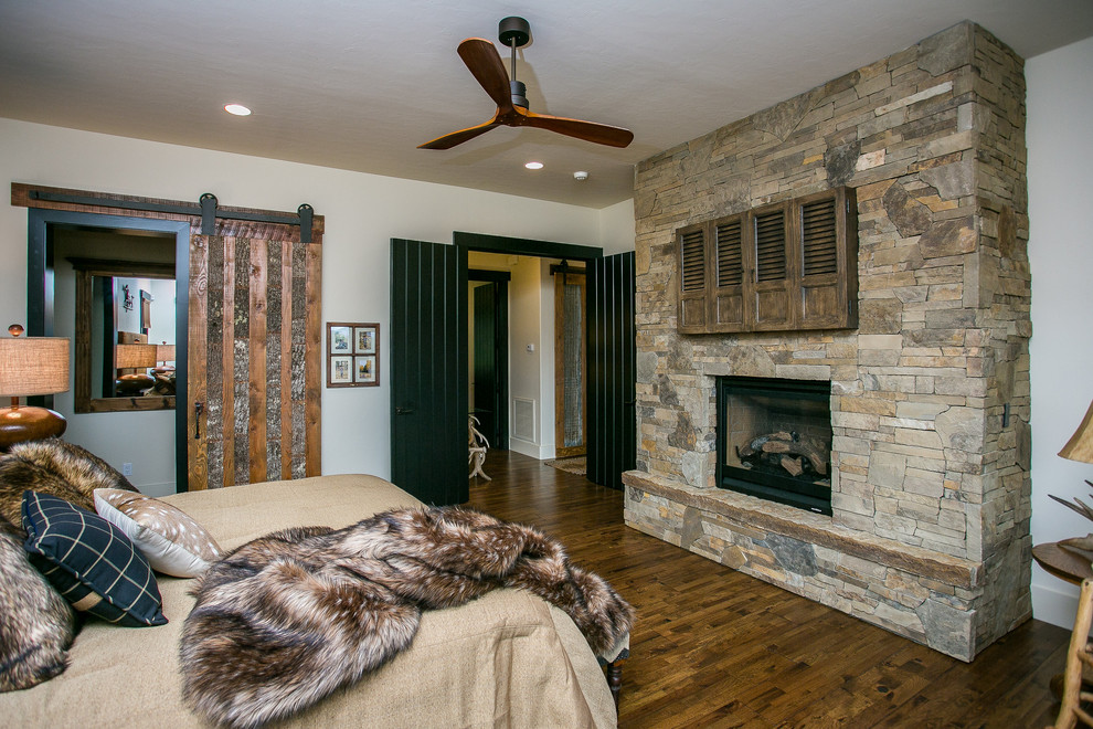 Inspiration for a large rustic master dark wood floor and brown floor bedroom remodel in Phoenix with white walls, a standard fireplace and a stone fireplace