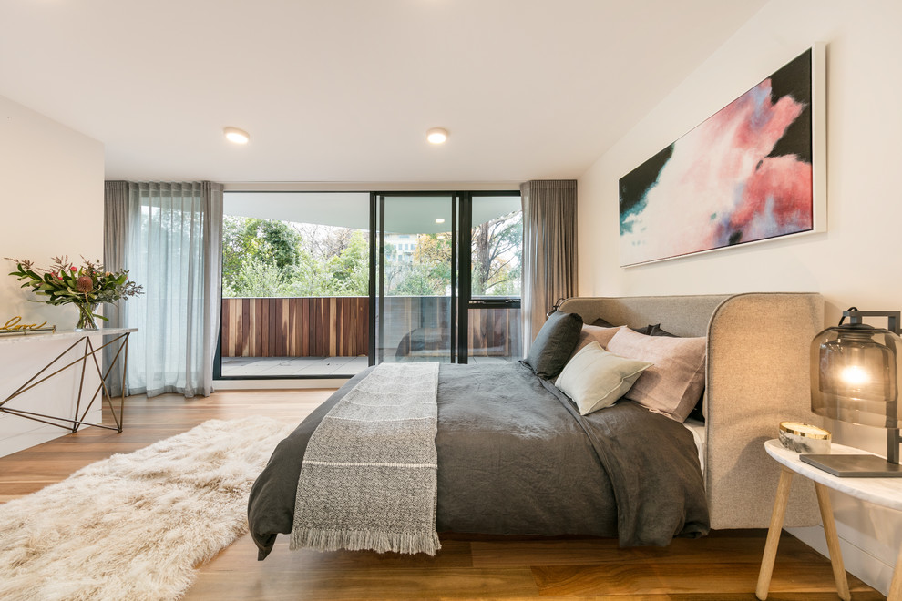 Contemporary master bedroom in Melbourne with white walls, medium hardwood flooring and brown floors.