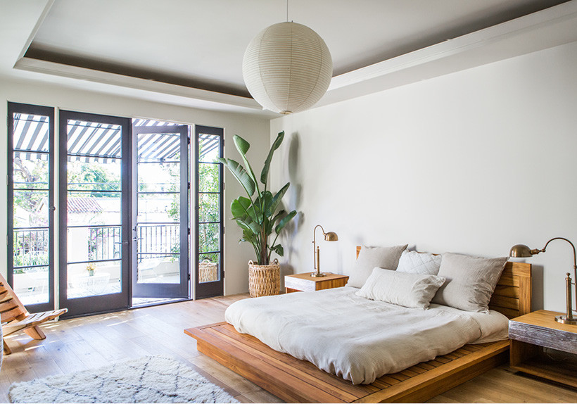 This is an example of an expansive contemporary master bedroom in Los Angeles with white walls and light hardwood flooring.