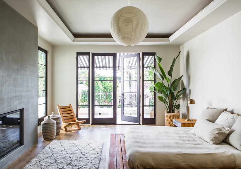 Geräumiges Modernes Hauptschlafzimmer mit weißer Wandfarbe, hellem Holzboden, Kaminumrandung aus Beton und Kamin in Los Angeles