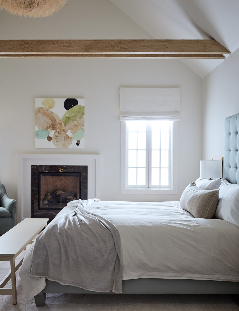 Diseño de dormitorio principal costero con paredes blancas, todas las chimeneas, marco de chimenea de madera y suelo beige