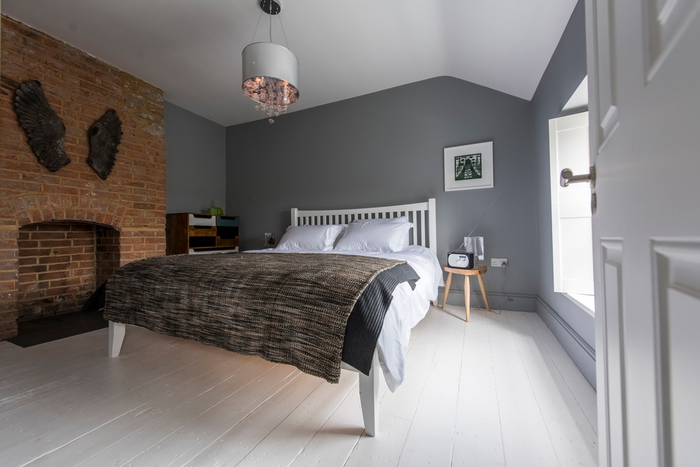 ロンドンにあるトランジショナルスタイルのおしゃれな客用寝室 (グレーの壁、塗装フローリング、標準型暖炉、レンガの暖炉まわり) のインテリア