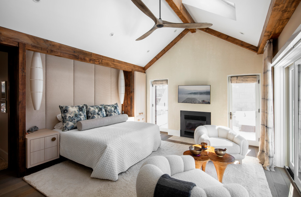 Ejemplo de dormitorio principal y abovedado marinero con paredes beige, suelo de madera oscura, chimenea lineal y vigas vistas