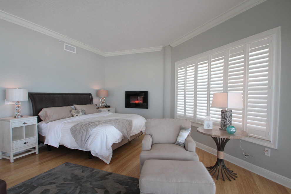 Mittelgroßes Maritimes Hauptschlafzimmer mit grüner Wandfarbe, hellem Holzboden, Kamin, Kaminumrandung aus Metall und grauem Boden in Tampa