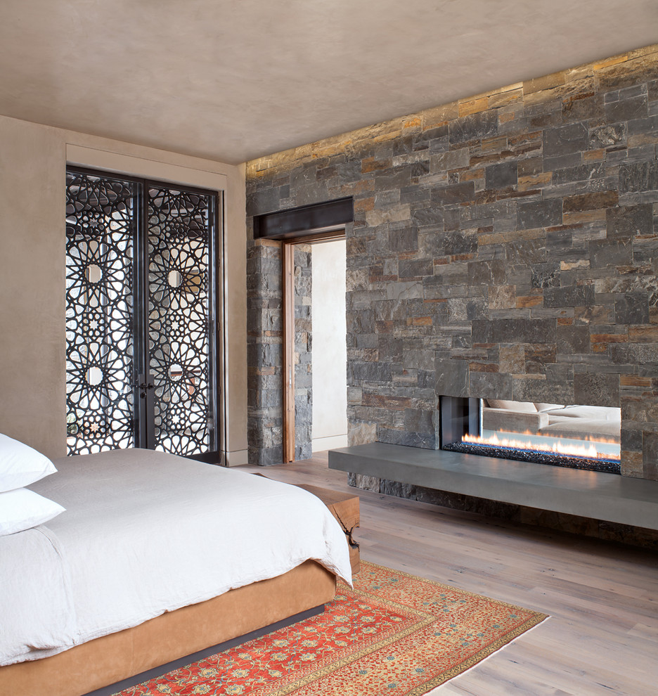 Идея дизайна: хозяйская спальня среднего размера в современном стиле с бежевыми стенами, светлым паркетным полом, двусторонним камином, фасадом камина из камня и бежевым полом