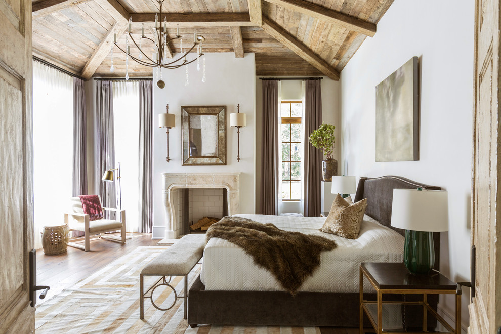 Mediterranes Hauptschlafzimmer mit weißer Wandfarbe, dunklem Holzboden, Kamin, Kaminumrandung aus Stein und braunem Boden in Houston