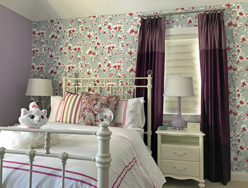 floral wallpaper with purple curtains and white bedding with purple stripe on a white iron bed