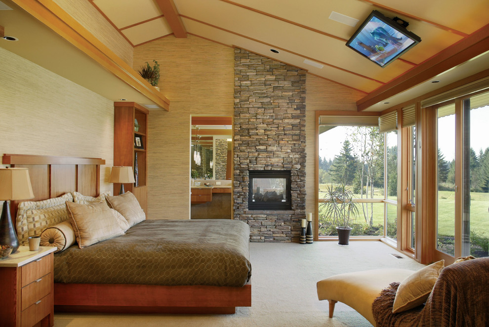 На фото: спальня в классическом стиле с фасадом камина из камня, двусторонним камином и телевизором с