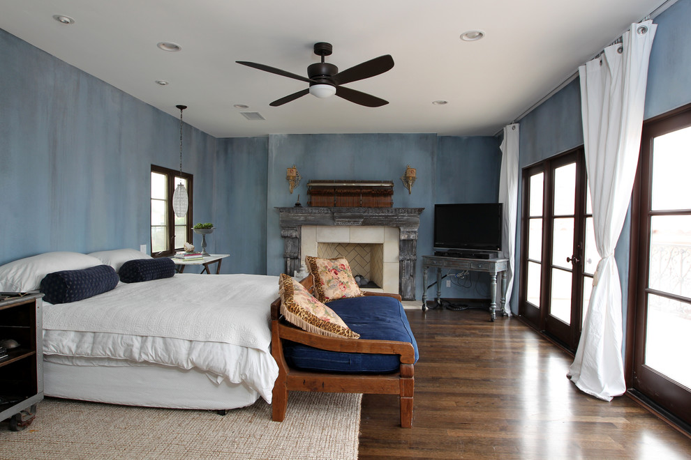 Geräumiges Uriges Hauptschlafzimmer mit blauer Wandfarbe, dunklem Holzboden, Kamin, Kaminumrandung aus Stein und braunem Boden in Los Angeles