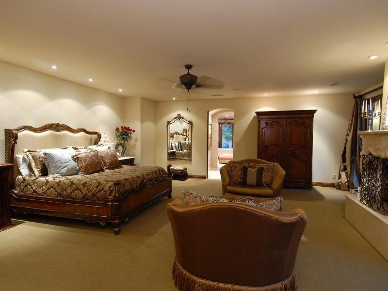 Пример оригинального дизайна: большая хозяйская спальня в средиземноморском стиле с бежевыми стенами, ковровым покрытием, стандартным камином и фасадом камина из камня