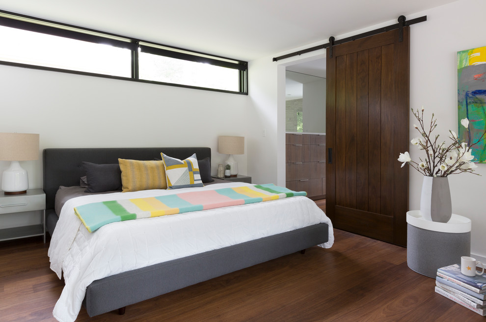 Cette photo montre une chambre tendance avec un mur blanc, parquet foncé et un sol marron.