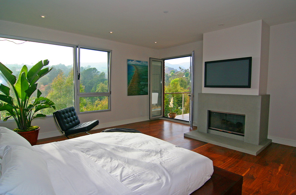 This is an example of a contemporary bedroom in Los Angeles with white walls, dark hardwood flooring and a standard fireplace.