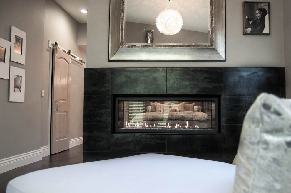 На фото: большая хозяйская спальня в классическом стиле с серыми стенами, темным паркетным полом, двусторонним камином, фасадом камина из плитки и коричневым полом с
