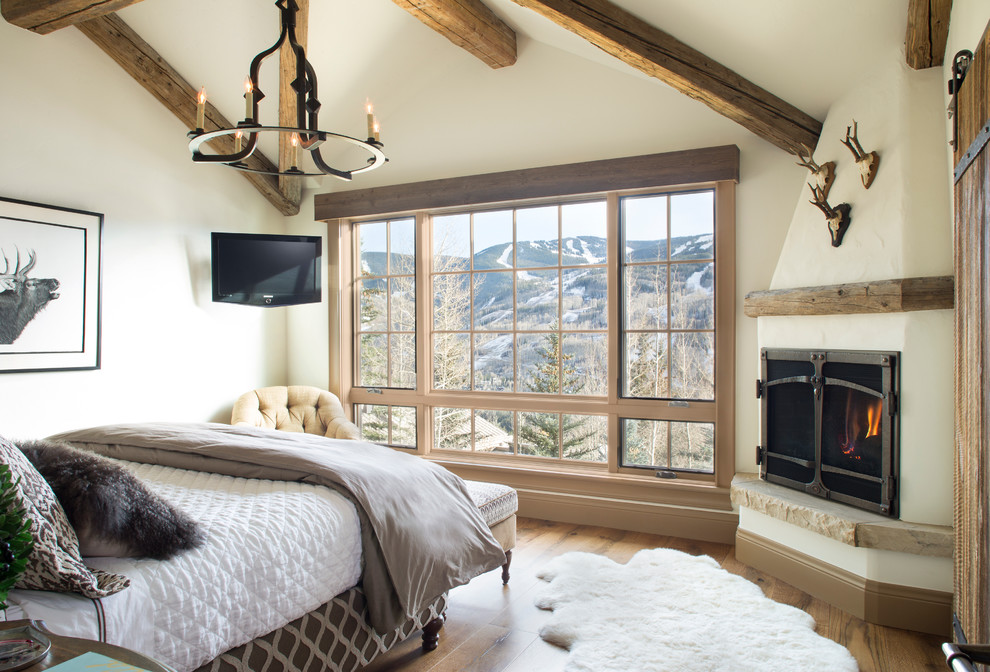 Ejemplo de dormitorio principal rural con paredes beige, suelo de madera en tonos medios y chimenea de esquina