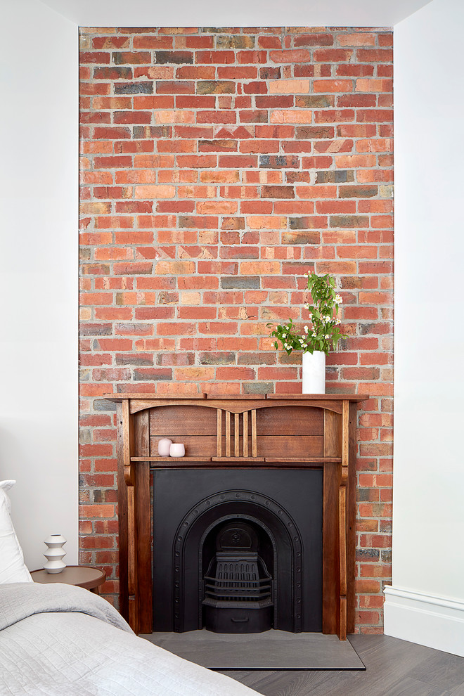 Inspiration pour une chambre d'amis design de taille moyenne avec un mur blanc, un sol en bois brun, une cheminée d'angle, un manteau de cheminée en brique et un sol gris.