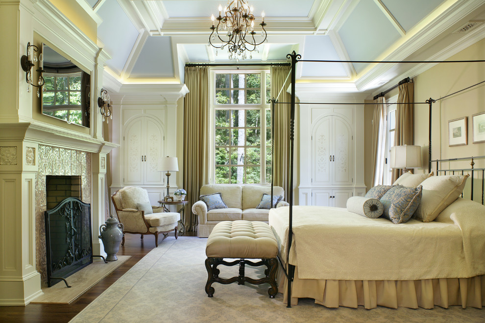 На фото: большая хозяйская спальня в классическом стиле с бежевыми стенами, темным паркетным полом, стандартным камином, фасадом камина из штукатурки и коричневым полом