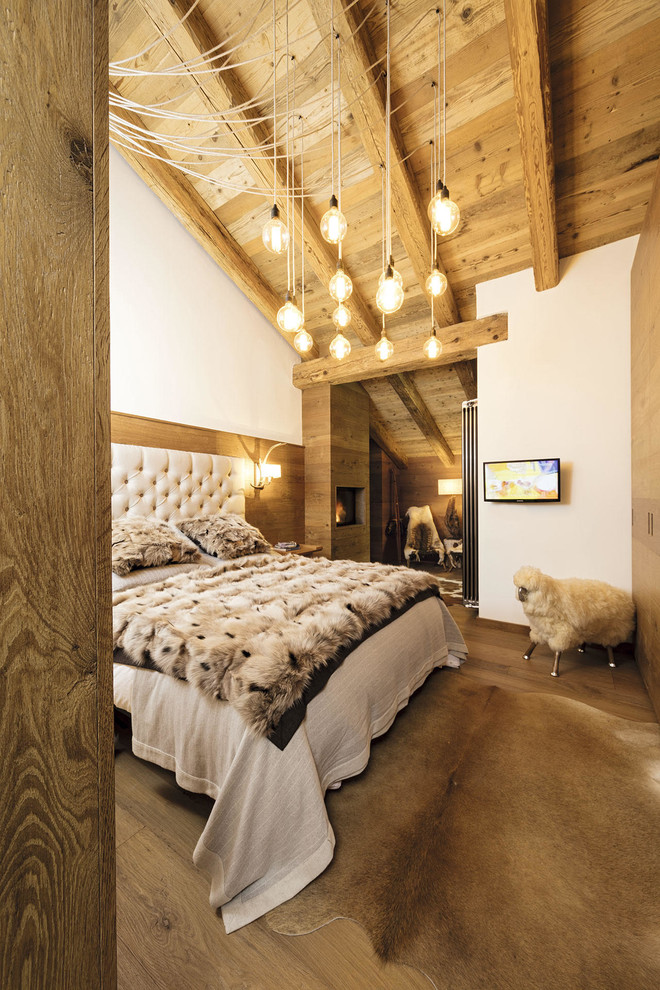 Cette image montre une petite chambre parentale chalet avec un mur blanc, un sol en bois brun, un sol marron, cheminée suspendue et un manteau de cheminée en bois.