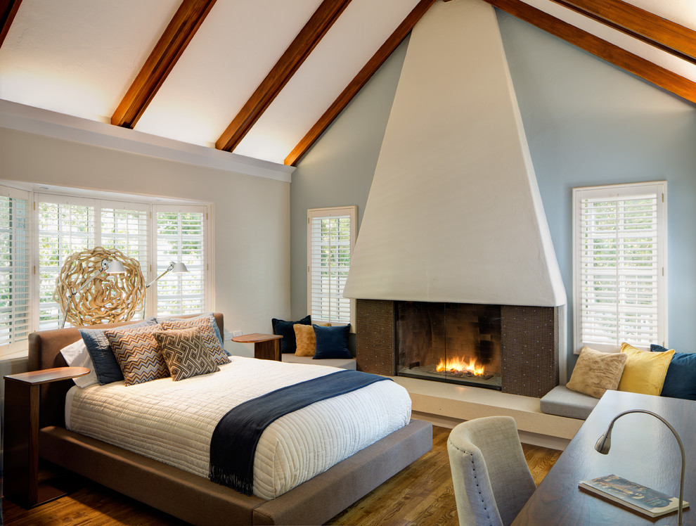 Imagen de dormitorio principal clásico renovado grande con paredes azules, suelo de madera en tonos medios, todas las chimeneas y marco de chimenea de yeso