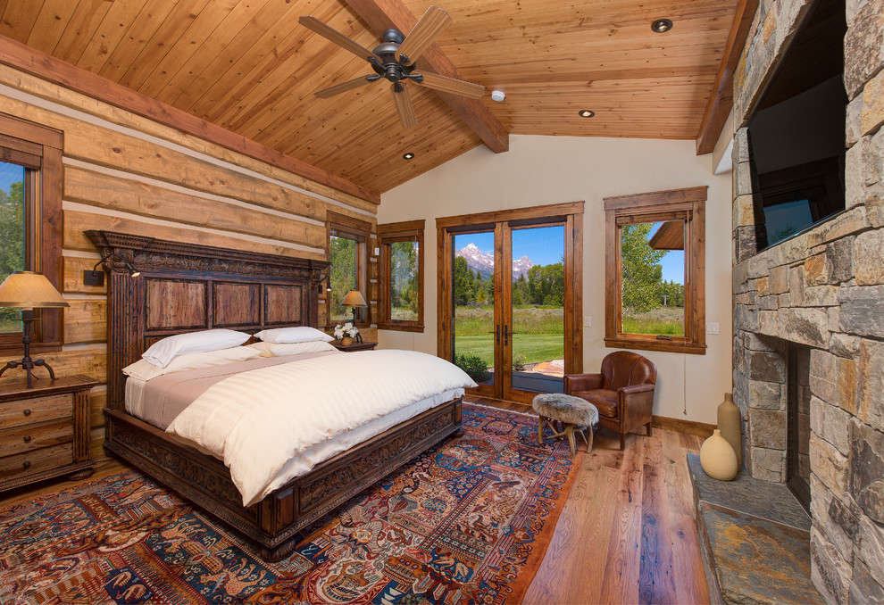 Imagen de dormitorio principal rústico con paredes beige, suelo de madera en tonos medios, todas las chimeneas y marco de chimenea de piedra