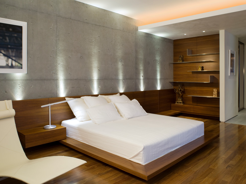 Aménagement d'une chambre parentale moderne de taille moyenne avec un mur gris, un sol en bois brun, cheminée suspendue et un sol marron.