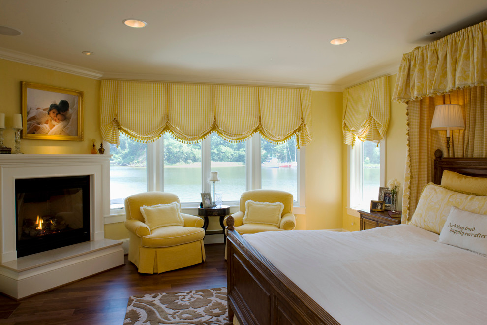 Klassisches Hauptschlafzimmer mit gelber Wandfarbe, braunem Holzboden und Eckkamin in Baltimore