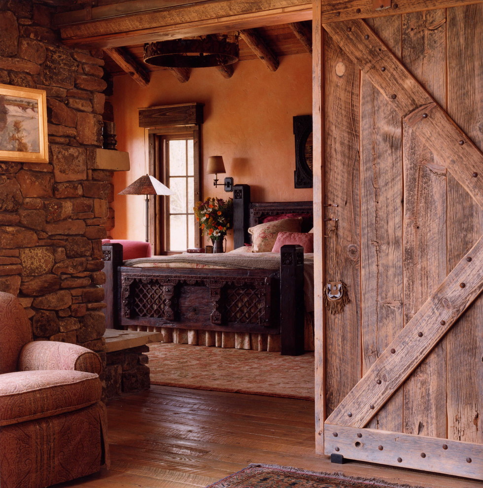Immagine di una grande camera da letto stile rurale con pavimento in legno massello medio, camino classico e cornice del camino in pietra