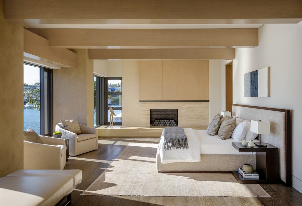 Modernes Hauptschlafzimmer mit weißer Wandfarbe, dunklem Holzboden, Kamin und Kaminumrandung aus Stein in Orange County